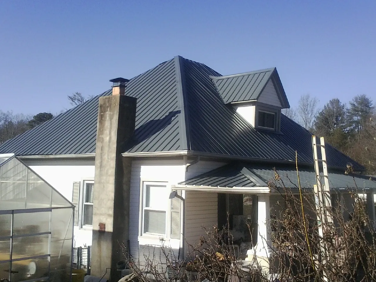 Dark blue standing seam metal roof on a white farmhouse with dormer — Slate & Tile Roof Repair by Roofing Brothers in Oak City