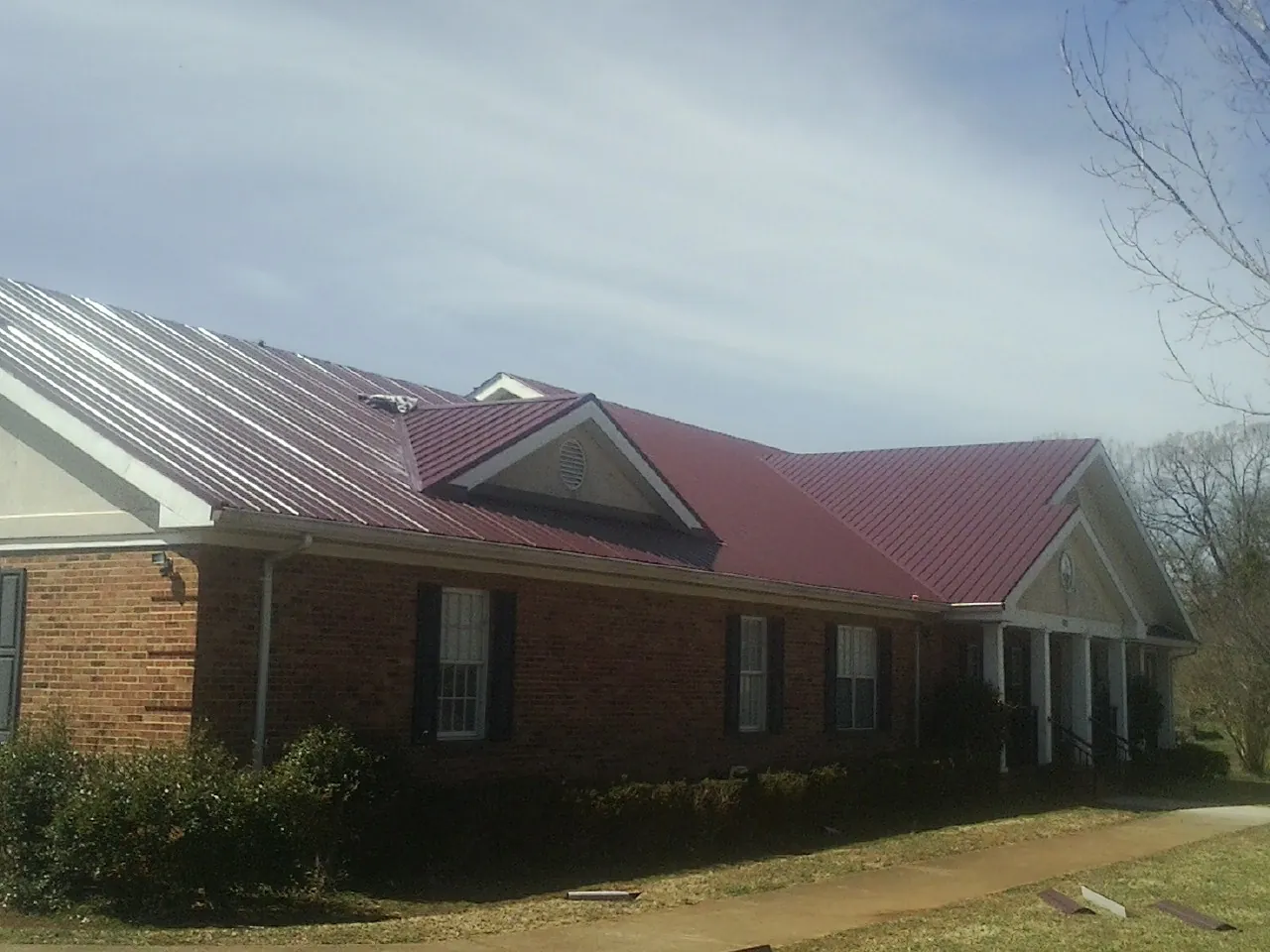 Red metal roof with gabled entries on a long brick building, from a Hail Damage Roof Repair job in Oak City
