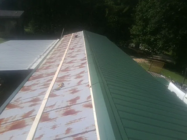 Old rusted panels beside newly installed green metal roofing — Wind Damage Roof Repair by Roofing Brothers in Oak City