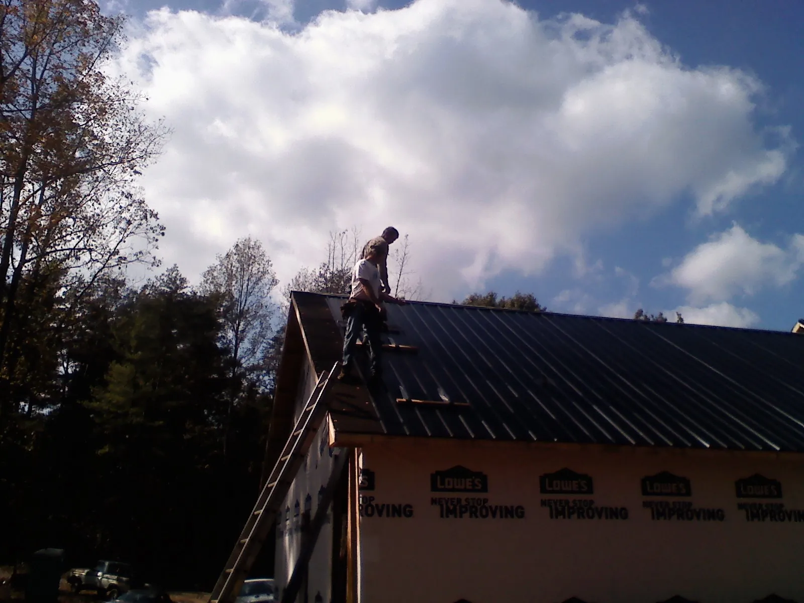 Roofer fastening dark metal panels high against a cloudy sky, from a Roof Inspection job in Oak City