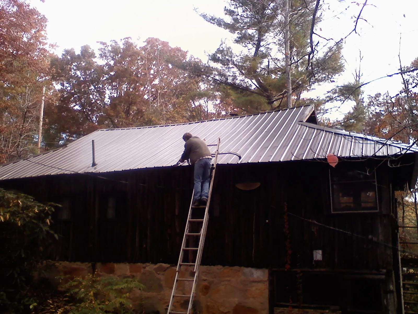 Roofer on a ladder working along the edge of a cabin metal roof in Oak City