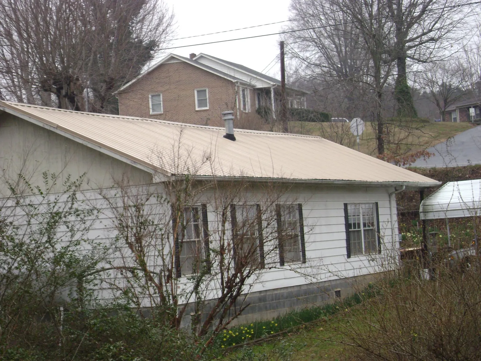 Tan metal roof on a white sided house set into a hillside — Commercial Roofing by Roofing Brothers in Oak City